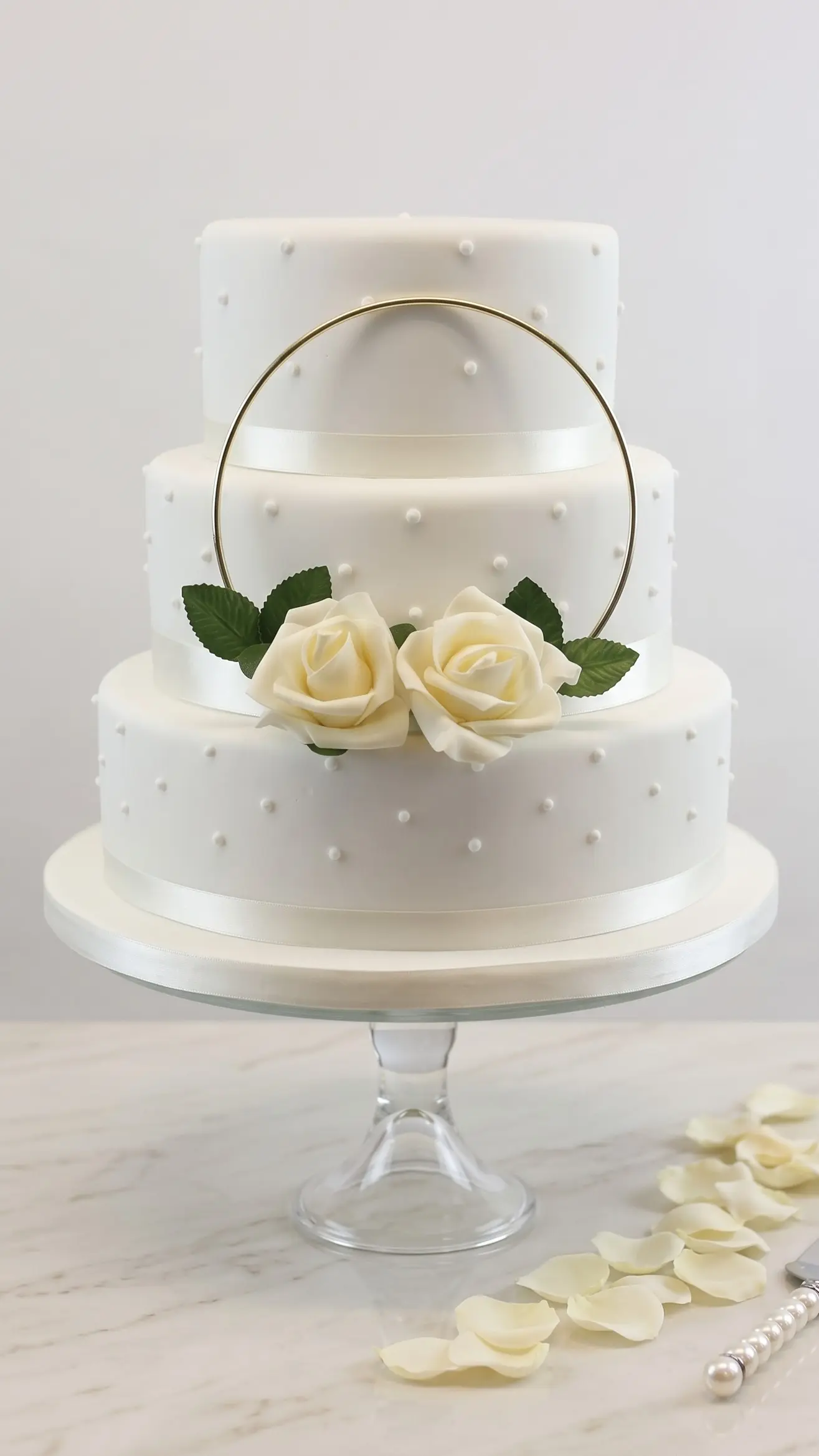 Classic three-tier white wedding cake with pearl details, white roses and gold hoop decoration